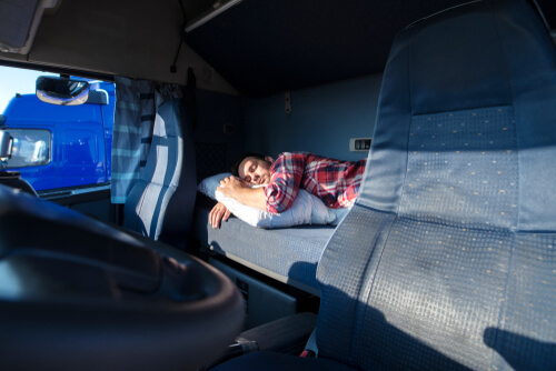 Truck driver sleeping in his cabin after working long routes overtime. Sleepy trucker taking a nap on a bed inside truck transporter. Lack of sleep.